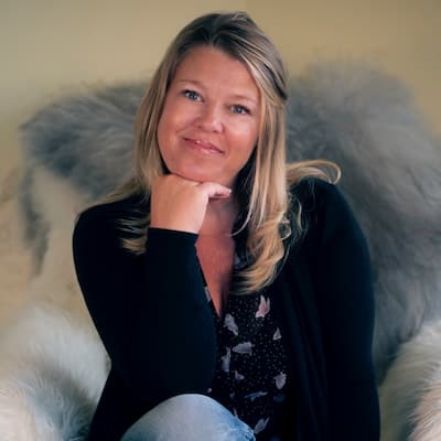 Julie Bacon smiling, sitting on cozy fur blanket, professional portrait.
