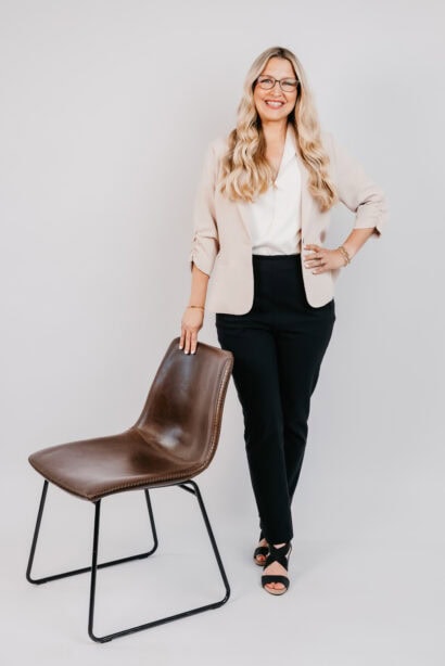 Businesswoman smiling, standing next to a chair, in a professional setting.
