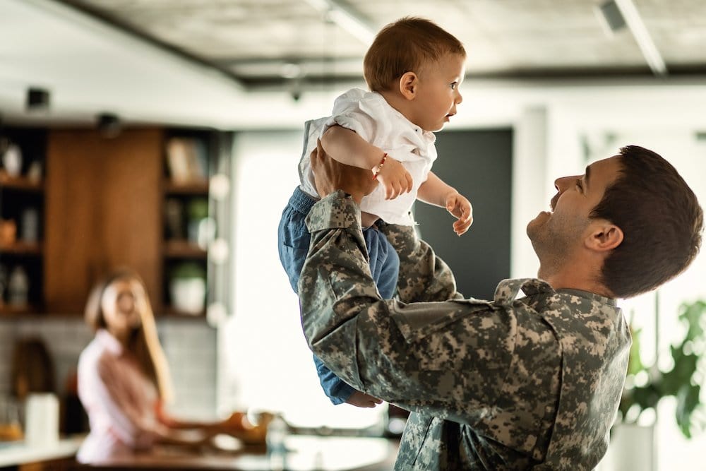 Father in military uniform lifting his young son, showcasing family support for VA loans.