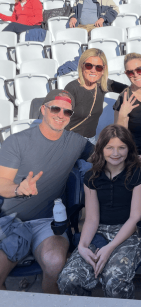 Family enjoying a sports event at a stadium with bright sunlight and cheerful expressions.