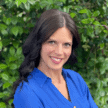 Portrait of Meredith Alexander smiling outdoors with greenery background.
