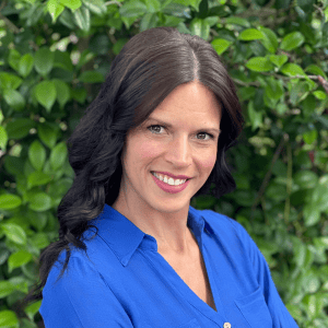 Portrait of Meredith Alexander smiling outdoors with greenery background.