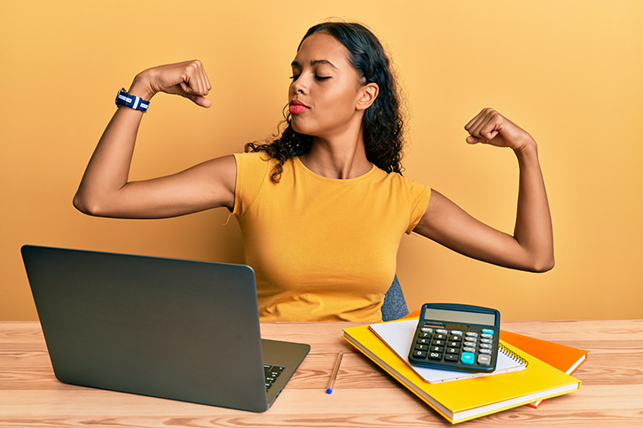 Young african american girl working at the office with laptop and calculator showing arms muscles smiling proud. fitness concept.