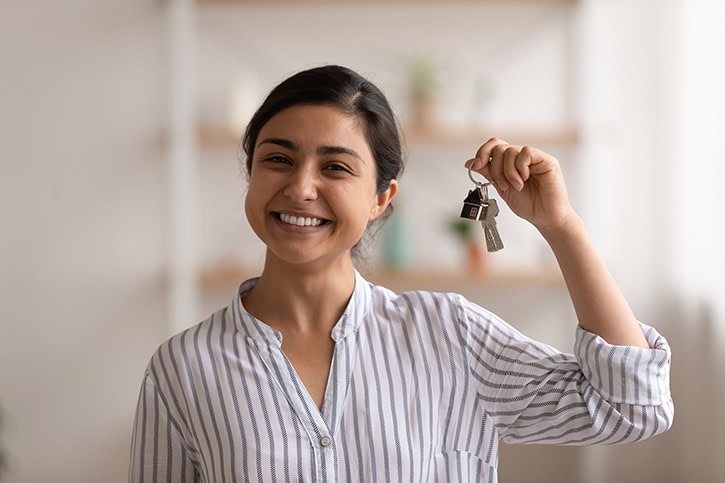 Happy woman holding house keys, saving for a home down payment.